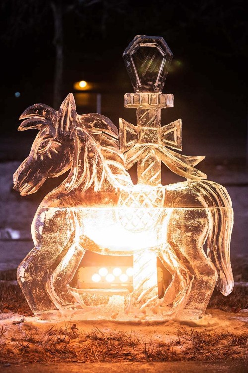 Illuminated ice sculpture of a horse beside a sword, showcasing intricate details and a warm glow.