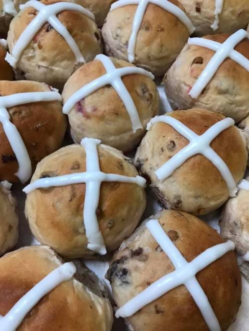 A close-up of freshly baked hot cross buns, topped with white icing crosses.