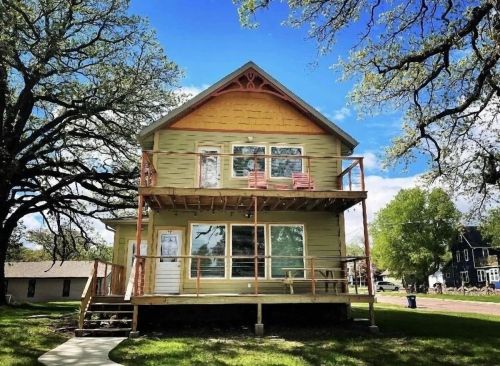 A two-story house with a wooden porch, surrounded by trees and a clear blue sky.