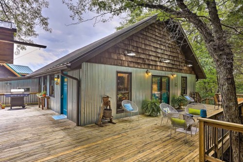 A cozy cabin with a metal exterior, surrounded by trees, featuring a wooden deck and outdoor seating.