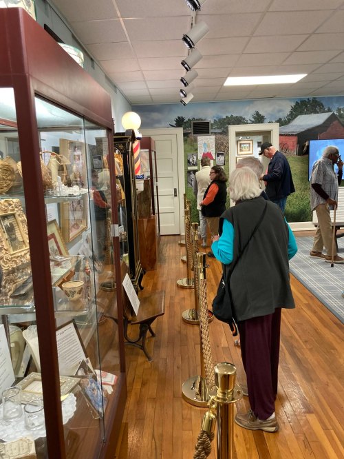 A museum interior with visitors observing exhibits behind a rope barrier, showcasing various artifacts and displays.