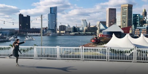 A person joyfully runs along a waterfront promenade with a city skyline in the background.