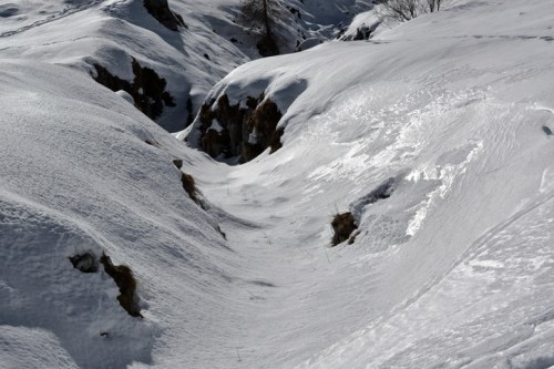 A snowy landscape with gentle slopes and a narrow valley, showcasing untouched white snow under bright sunlight.