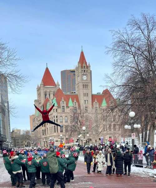 A lively winter parade scene with performers jumping in front of a historic building, surrounded by a festive crowd.