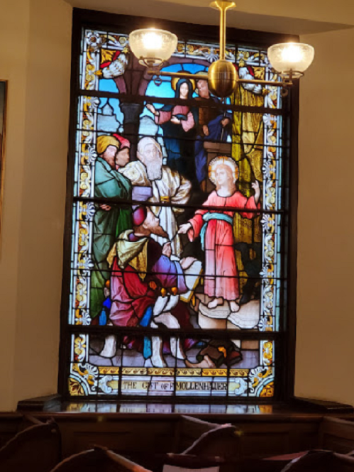 Stained glass window depicting a biblical scene with figures in colorful robes and intricate details.