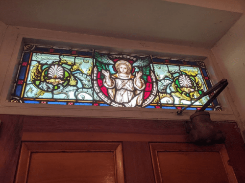 Stained glass window featuring an angel surrounded by colorful floral designs above a wooden door.