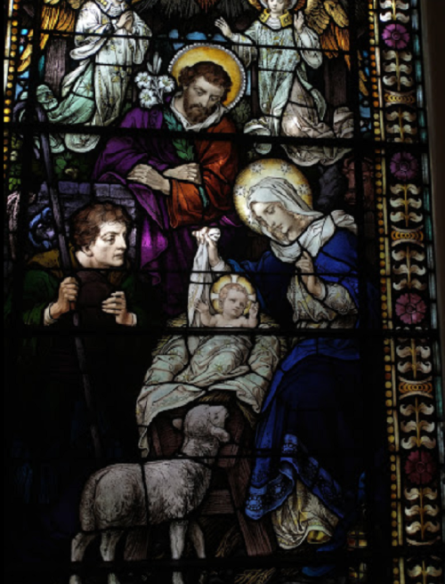 Stained glass depicting the Nativity scene with Mary, Joseph, baby Jesus, and angels. A shepherd and sheep are present.