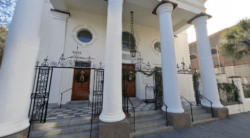 Historic building with white columns, double doors, and festive decorations, featuring a patterned stone walkway.