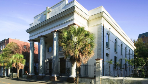 Historic building with columns and palm trees, set against a clear blue sky.