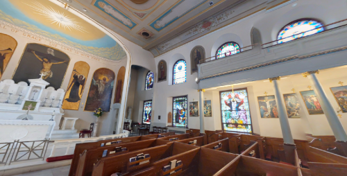 Interior of a church featuring stained glass windows, wooden pews, and a decorative altar with religious artwork.