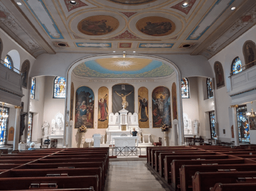 Interior of a church featuring an altar, stained glass windows, and decorative ceiling murals.