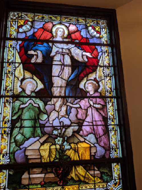 Stained glass window depicting a figure surrounded by angels, with vibrant colors and intricate designs.