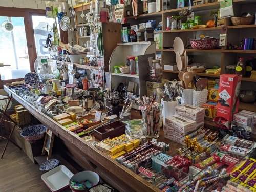 A cozy shop interior filled with various kitchenware, snacks, and household items on wooden shelves and tables.