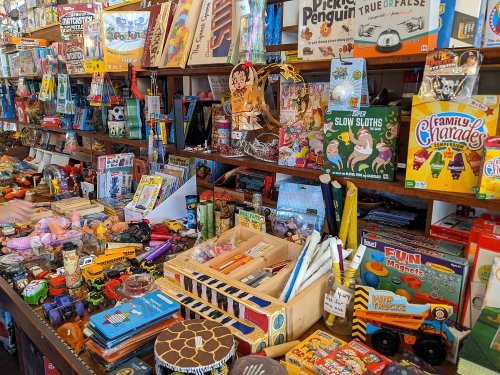 A colorful display of various toys and games on shelves and tables, creating a vibrant, cluttered atmosphere.
