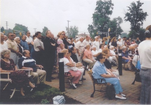 A large crowd of elderly people gathered outdoors, seated and standing, in a park-like setting.