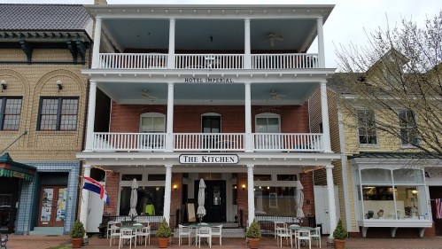 A three-story building with balconies, featuring "Hotel Imperial" and "The Kitchen" signs, surrounded by outdoor seating.