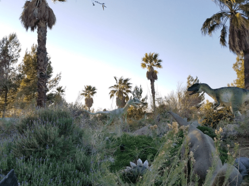 A lush garden scene featuring dinosaur sculptures among palm trees and greenery.