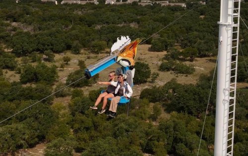 Two people enjoy a thrilling ride on a zip line above a green landscape with trees.