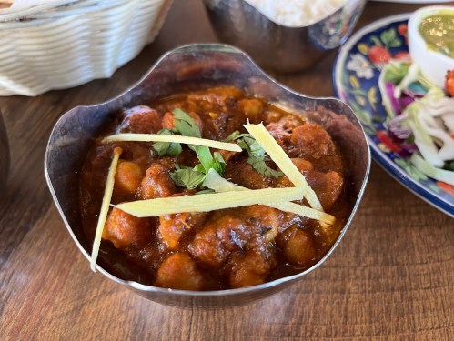 A bowl of spicy chickpea curry garnished with ginger and cilantro, served with rice and side dishes.