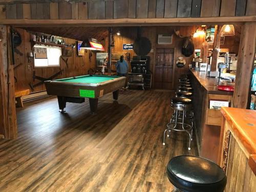 A rustic bar interior featuring a pool table, wooden walls, and stools along the counter.