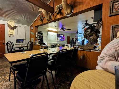 A rustic diner interior with wooden walls, tables, and mounted animal decor, including a large turkey statue.