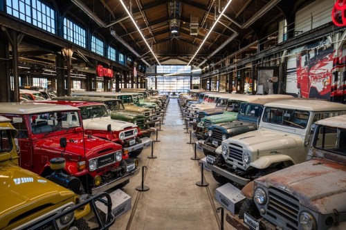 A spacious museum showcasing a row of vintage Toyota trucks and SUVs under bright industrial lighting.