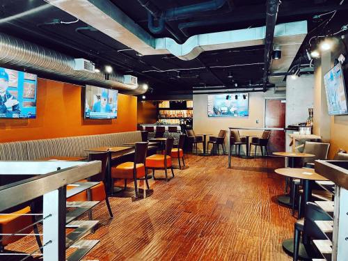 A modern bar interior with wooden floors, tables, and multiple TVs displaying sports. Cozy seating along the walls.