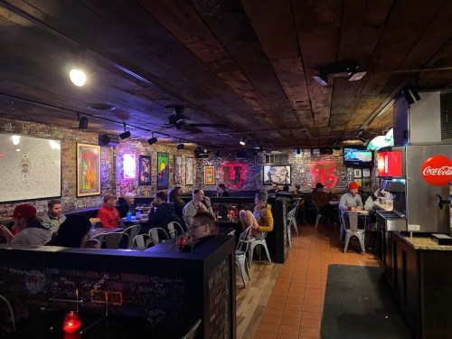 A lively bar scene with patrons seated at tables, colorful artwork on the walls, and a warm, inviting atmosphere.