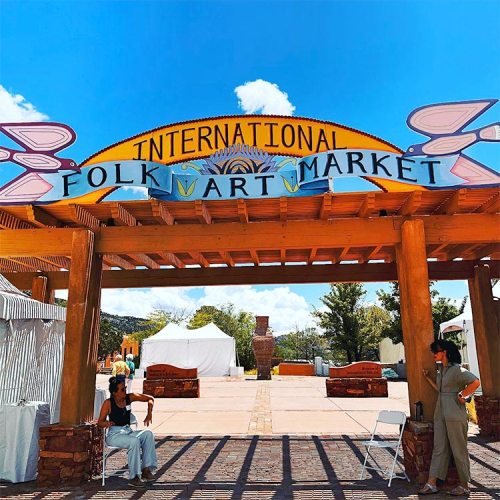 Entrance to the International Folk Art Market, featuring colorful signage and tents under a bright blue sky.