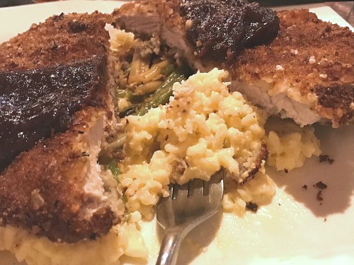 A plate with a breaded chicken cutlet stuffed with vegetables, served with creamy risotto and a fork.