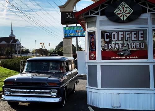 A vintage truck parked by a coffee drive-thru kiosk with a church steeple in the background.