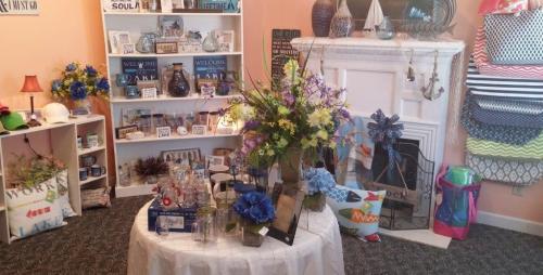 A cozy shop interior featuring a display of flowers, home decor items, and colorful accessories on shelves and tables.