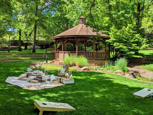 A serene park scene featuring a gazebo surrounded by greenery and a picnic setup on the grass.