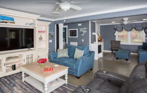 Cozy living room with blue furniture, a TV unit, and a coffee table, featuring light walls and a ceiling fan.