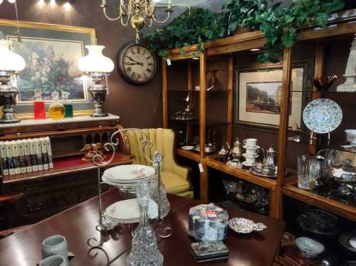 A cozy antique shop featuring vintage furniture, decorative items, and a collection of glassware and tableware.