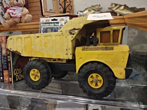 A vintage yellow toy dump truck displayed in a glass case, showing signs of wear and age.