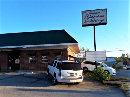 Exterior of Italian Garden Dining restaurant with a green roof and a sign, featuring parked cars in the lot.