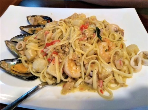 A plate of seafood pasta with shrimp, mussels, and calamari in a creamy sauce, garnished with herbs.