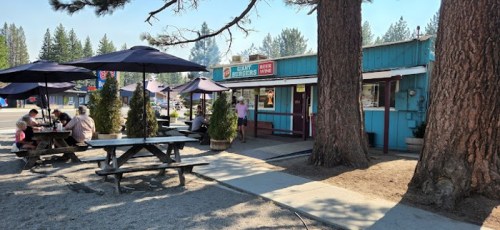 A colorful restaurant with outdoor seating under umbrellas, surrounded by trees and a gravel path.
