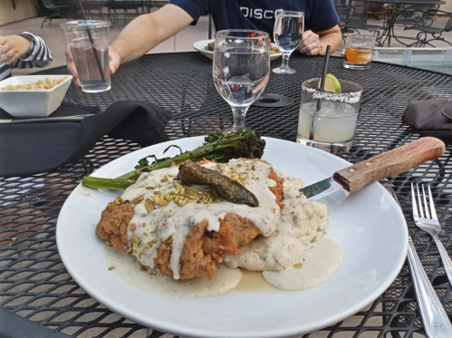 A plate of fried chicken with creamy sauce and sides, set on a table with drinks and other dishes in the background.