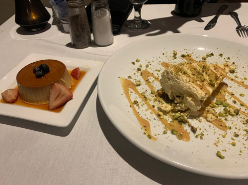 A dessert plate featuring flan with strawberries and a fluffy cake drizzled with caramel and sprinkled with pistachios.