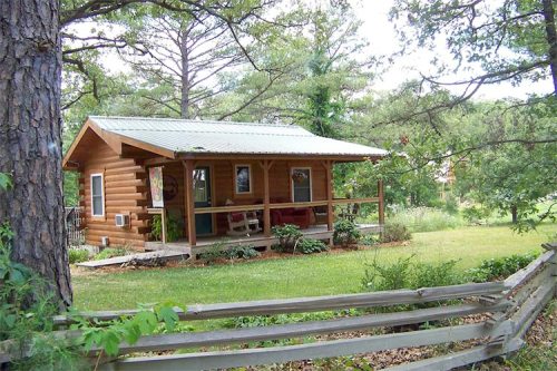A cozy log cabin with a porch, surrounded by trees and greenery, set in a peaceful outdoor landscape.