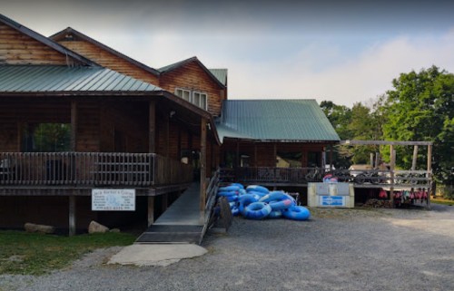 A rustic wooden building with a green metal roof, featuring a ramp and blue inner tubes stacked outside.