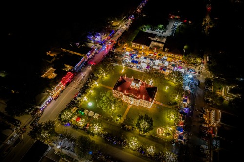 Aerial view of a festive night scene with colorful lights, a central building, and bustling market stalls.