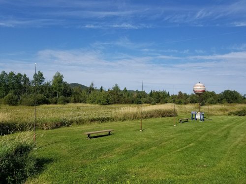A grassy field with benches, trees, and a water tower under a clear blue sky.