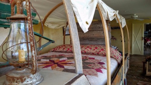 A cozy bed with a quilt, framed by a wooden wagon-like structure and an antique lantern nearby.