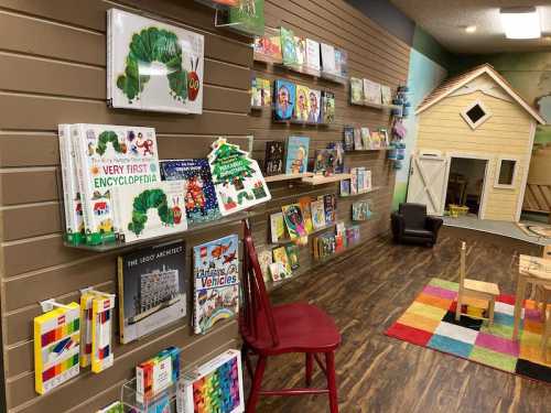 A cozy children's reading area with bookshelves, a red chair, and a colorful rug near a playhouse.