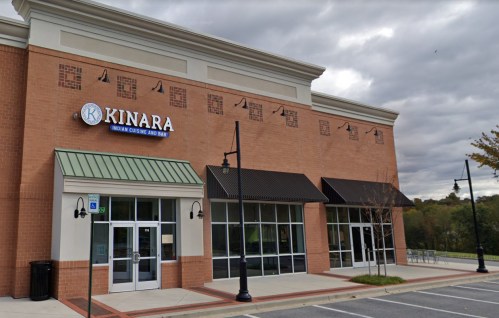 Exterior view of a restaurant named "Kinara," featuring a brick facade and large windows under a cloudy sky.