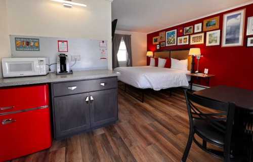 Cozy hotel room featuring a kitchenette, a queen bed, and colorful wall art. Modern decor with wooden flooring.