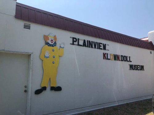 A colorful clown figure on the wall of the Plainview Klowndoll Museum, with the museum's name displayed above.